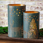 Two dark green lanterns with gold deer, forest and star cutouts glowing on a wood shelf