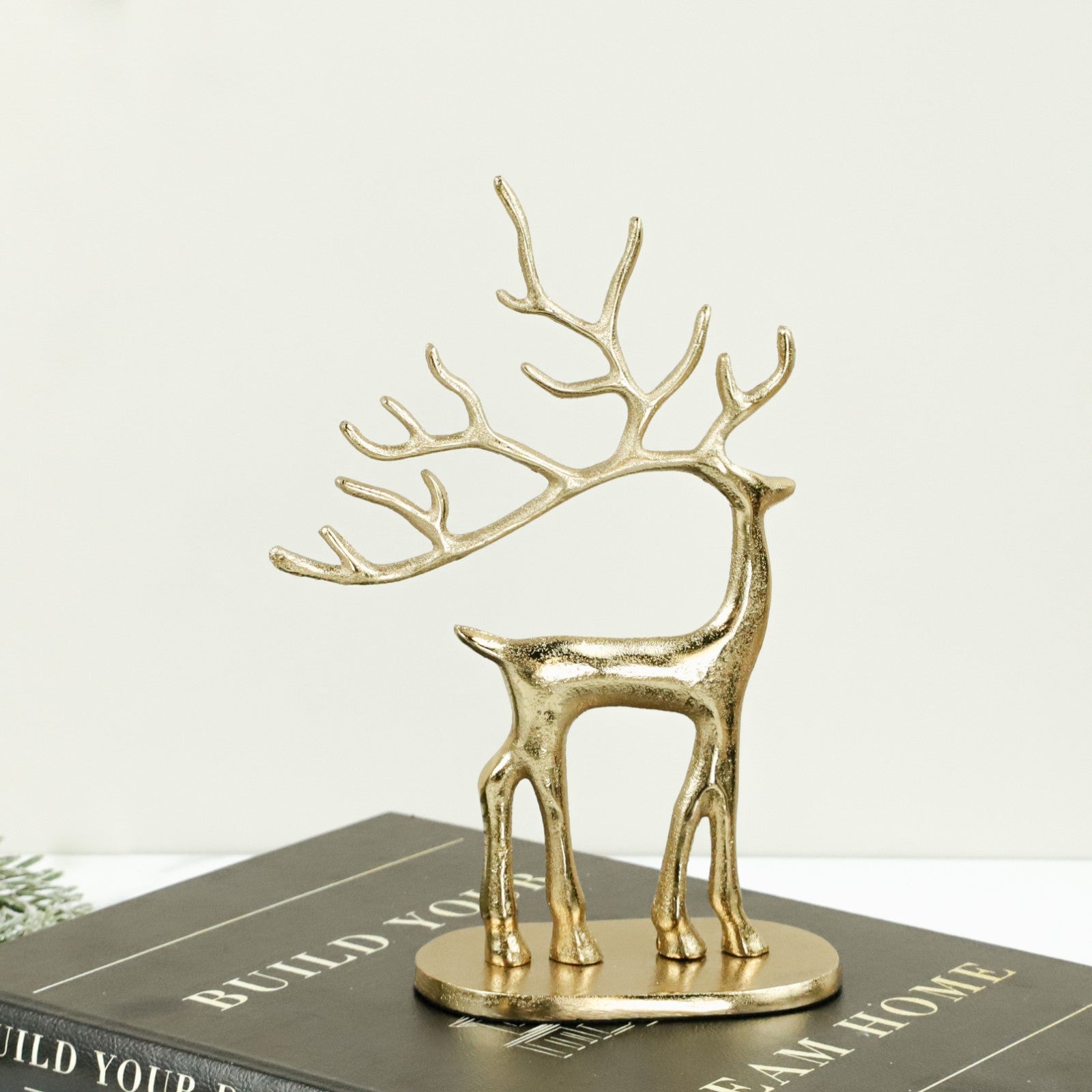 Gold metal reindeer with tall branching antlers on an oval base, standing on a stack of books