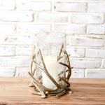 Clear glass hurricane on a gold antler base with a white pillar candle inside, on a wood table