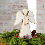 White wood angel with natural wood edges and a twine bow, set in fresh greenery with pinecones