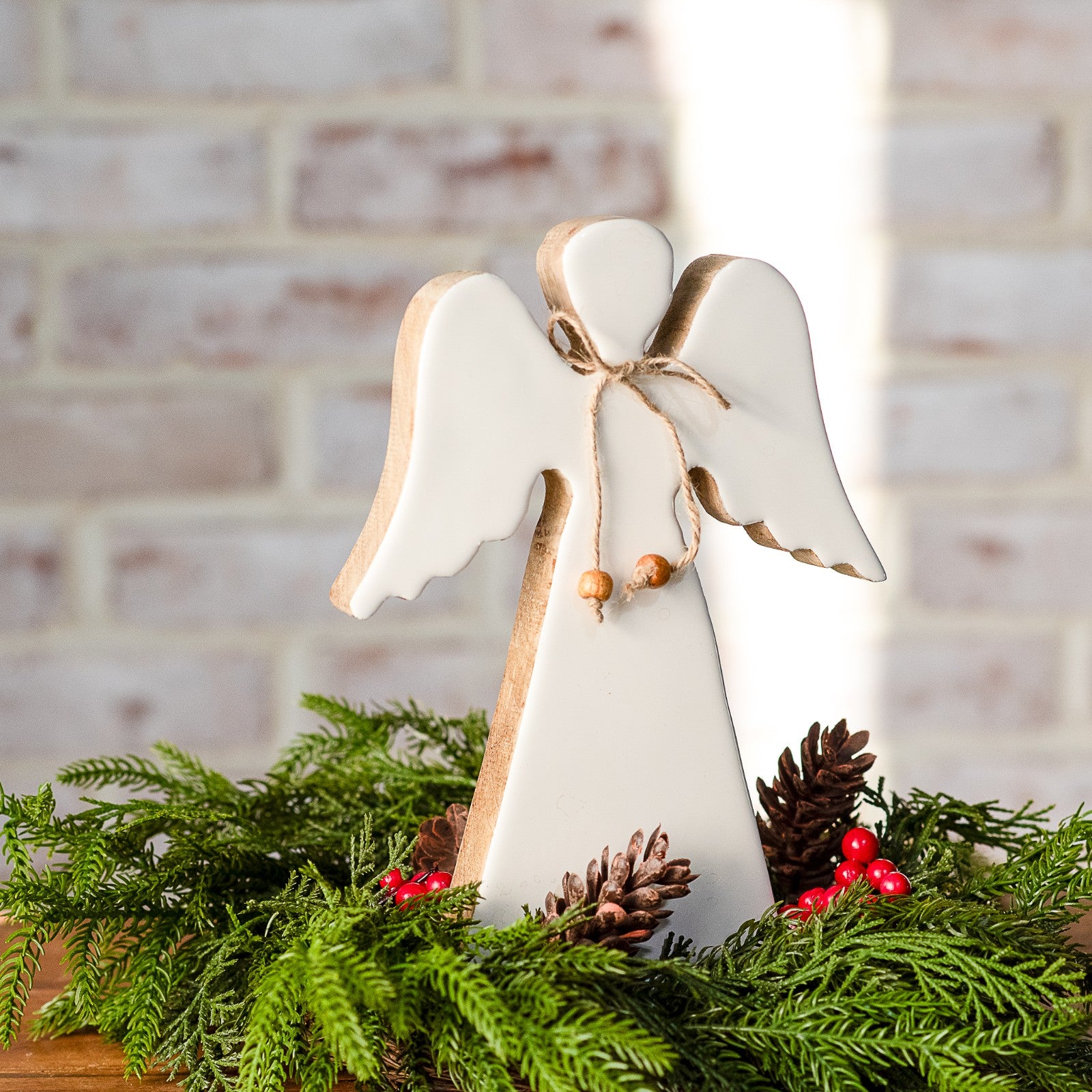 White wood angel with natural wood edges and a twine bow, set in fresh greenery with pinecones