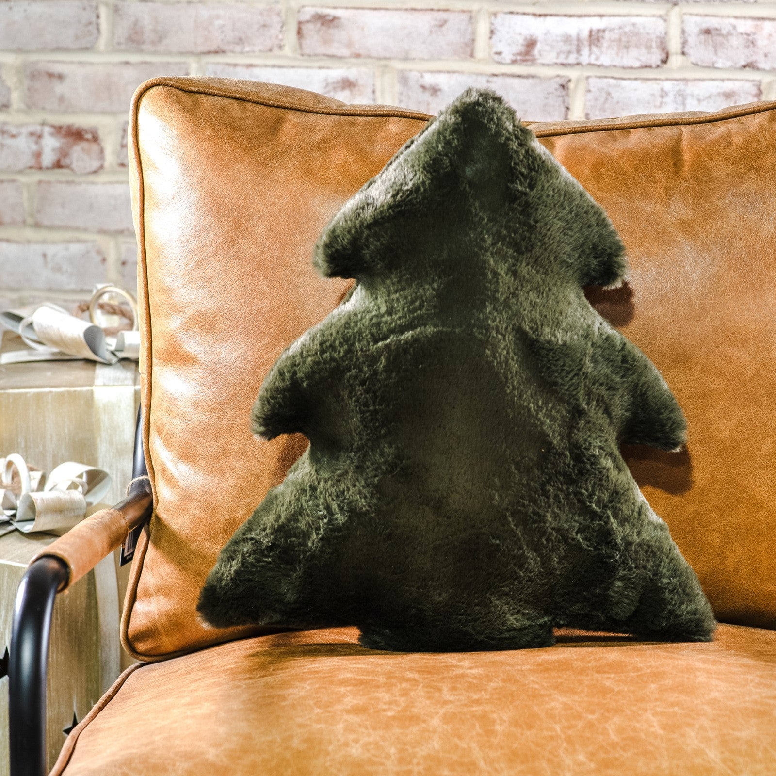 Dark green faux fur Christmas tree-shaped pillow on a cognac leather chair
