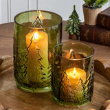 Two green glass hurricanes embossed with evergreen trees, each holding a lit pillar candle
