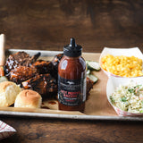 Grilled short ribs with rolls, mac and cheese, pickles and coleslaw beside Hot Pepper Bacon Grill & Wing Sauce
