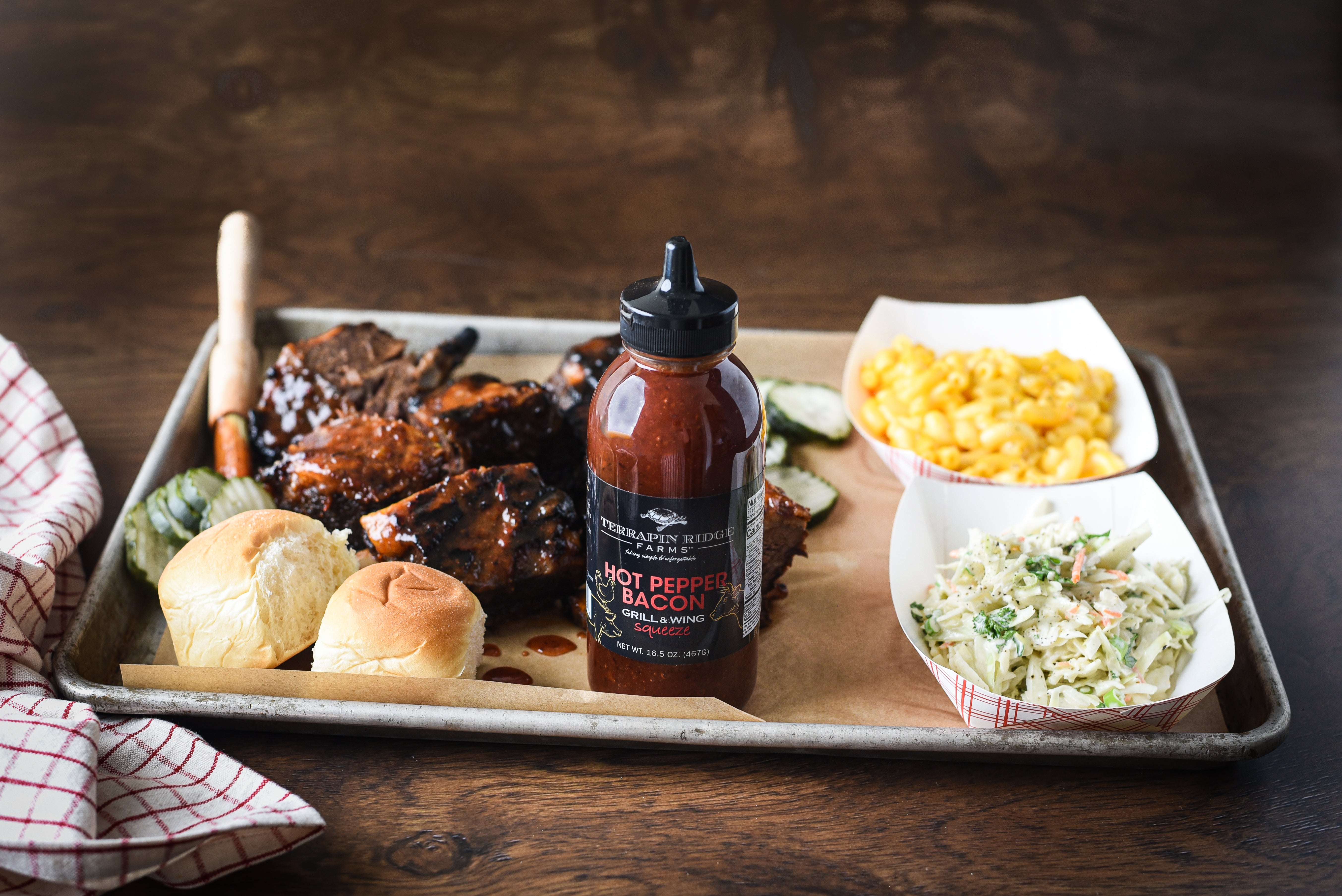Grilled short ribs with rolls, mac and cheese, pickles and coleslaw beside Hot Pepper Bacon Grill & Wing Sauce