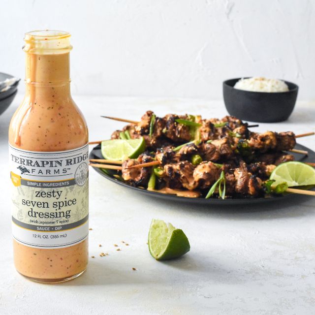 Grilled steak skewers with lime wedges and rice beside Zesty Seven Spice Dressing