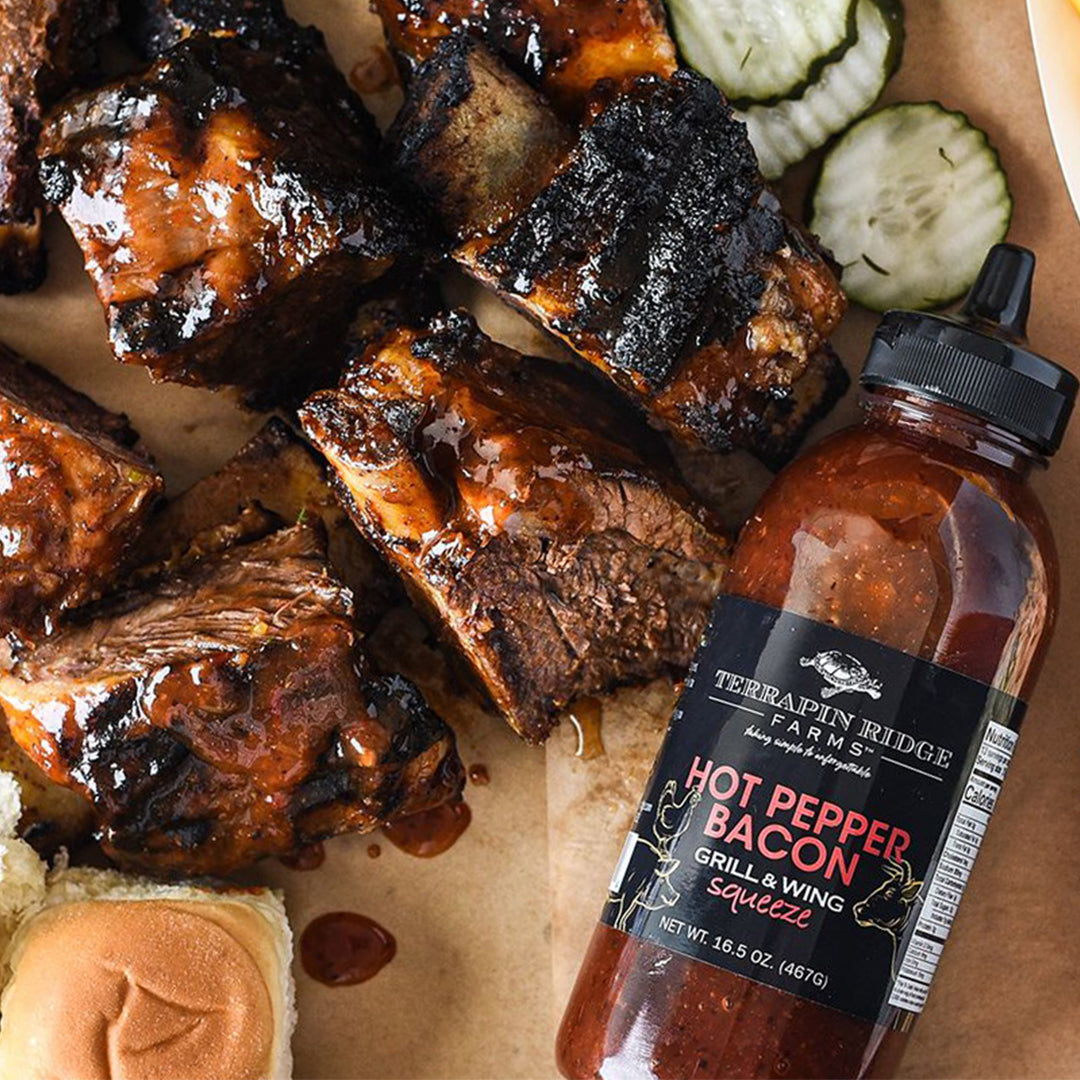 Saucy grilled ribs with pickles and bread next to Hot Pepper Bacon Grill & Wing Sauce