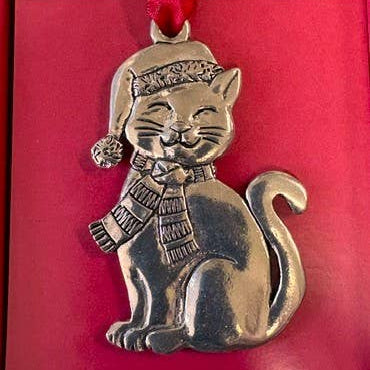 Pewter cat in a scarf and knit hat hanging from red ribbon in a red gift box with ornament print