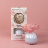 Sweet Grace Flower Diffuser white ceramic base with pink flower in front of pastel pink floral packaging