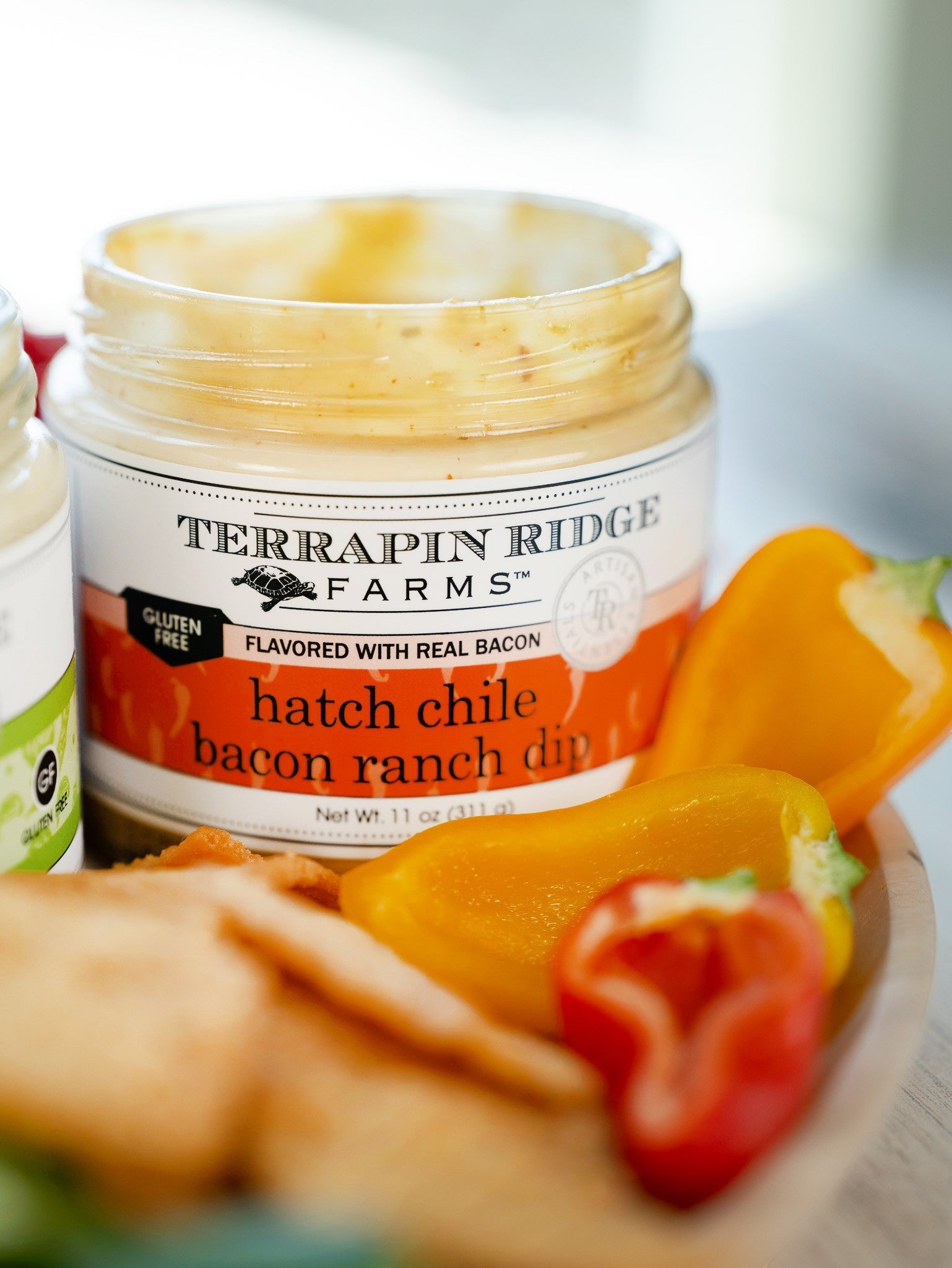 Open jar of Hatch Chile Bacon Ranch Dip with sliced bell peppers and crackers