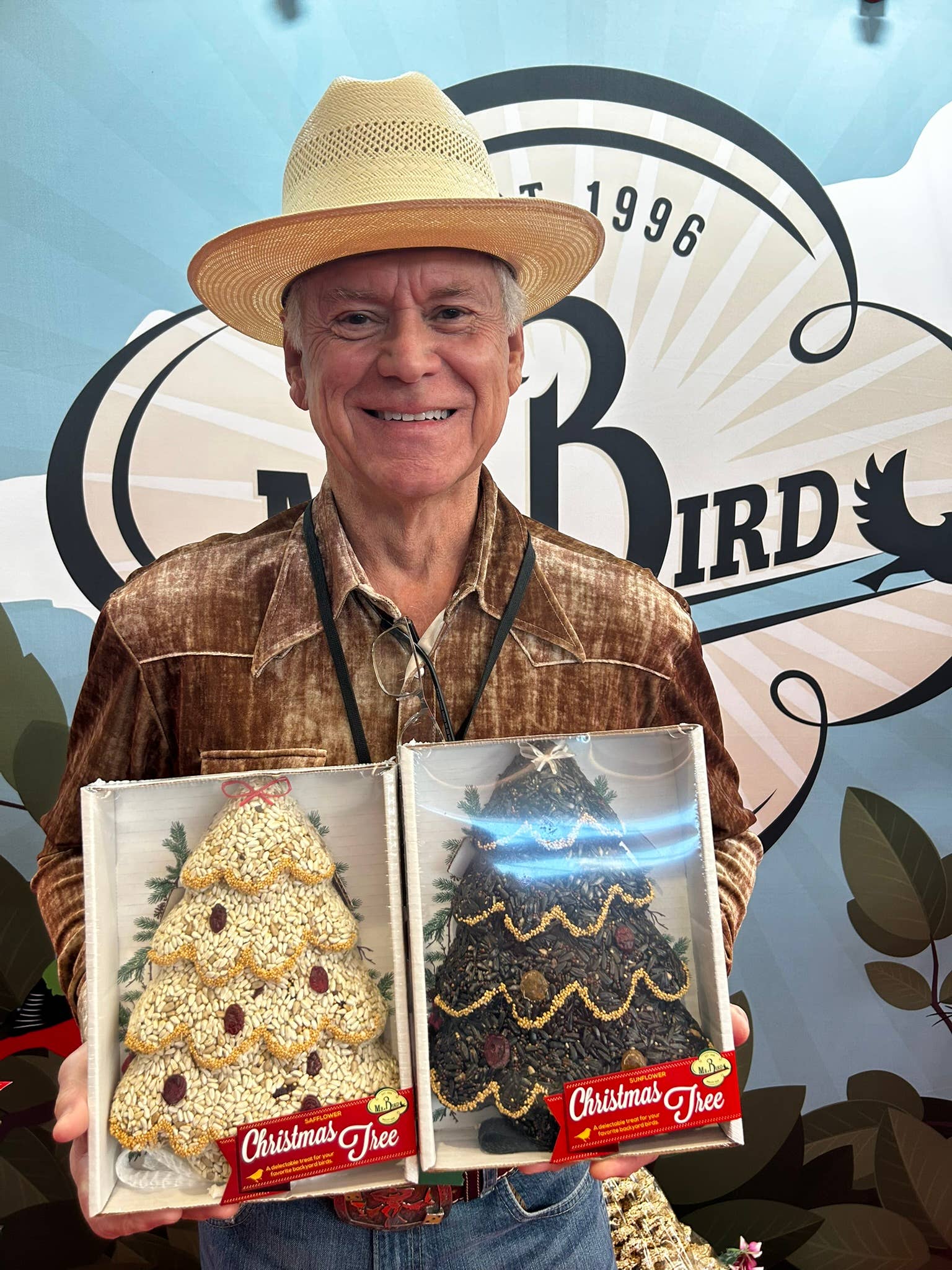 Man in a straw hat holding two boxed bird seed Christmas trees