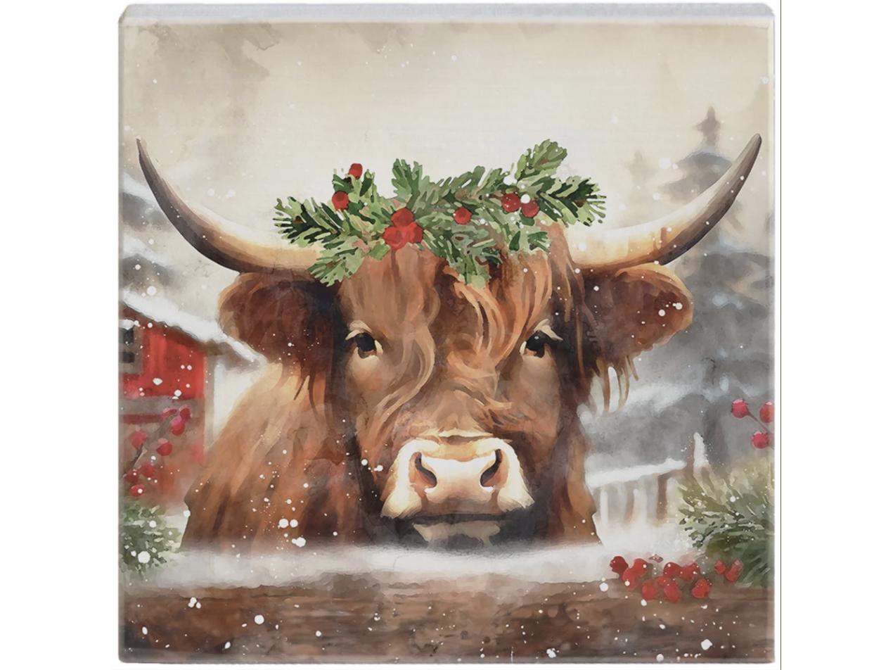 Small square block sign of a Highland cow in a holly crown beside a red barn