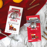 Two mulling spice boxes with striped ribbons and tea ball infusers on a red cloth with cinnamon sticks