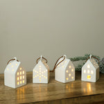 White ceramic LED house ornaments glowing on a wood shelf