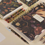 Spiral-bound art journal with a Forest Flowers illustrated cover, interior pages