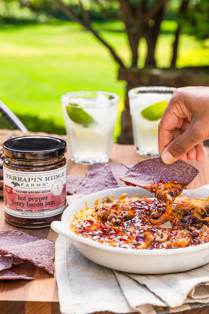 Baked cheese dip topped with Hot Pepper Berry Bacon Jam served with blue corn chips